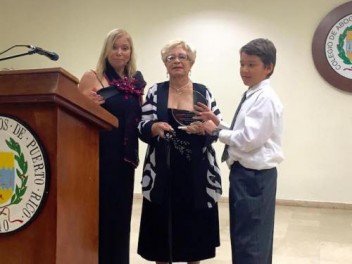 La dominicana Estebanía García recibe su reconocimiento de manos del niño Philip Berrios. Le acompaña Mery D’costa de la Coalición de Inmigrantes.